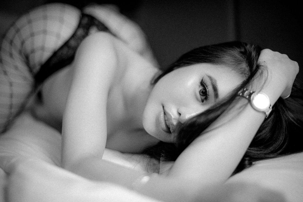 Konstnärligt svartvitt boudoirporträtt av mörkhårig kvinna i sängen