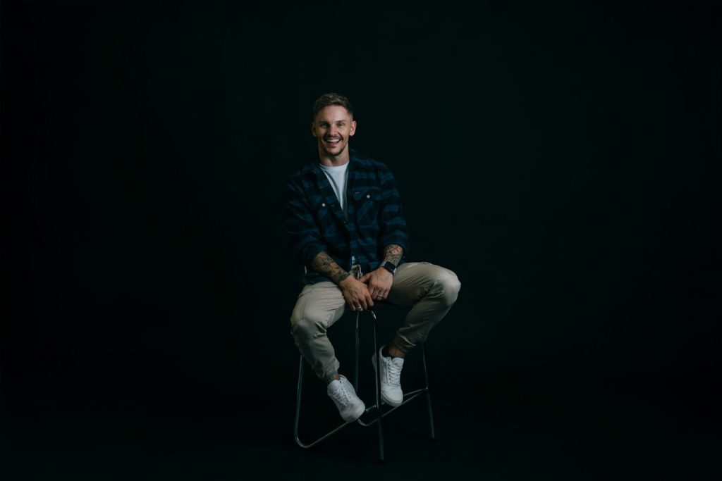 Leende man sitter på pall mot helt svart bakgrund