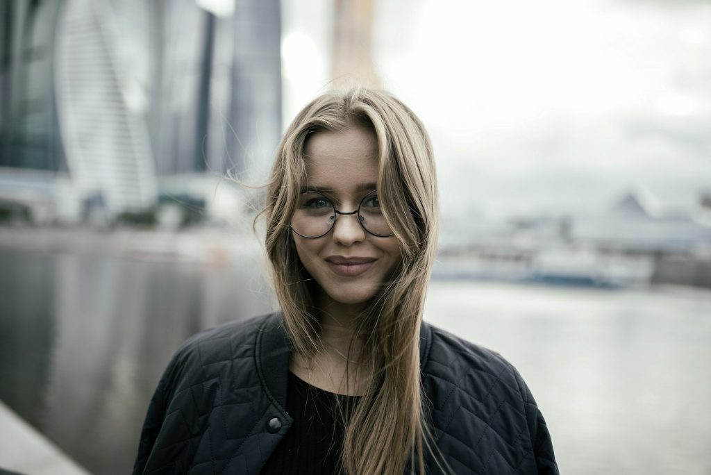 Leende ung kvinna med glasögon och långt ljust hår i staden