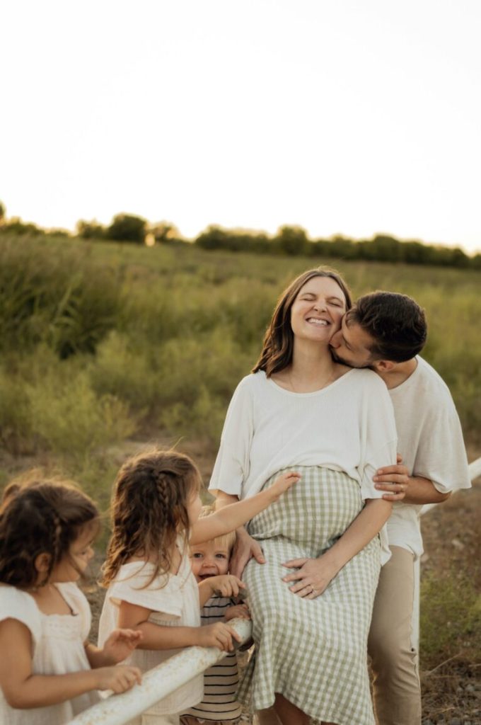 Familj med gravid mamma och döttrar på äng i solnedgång