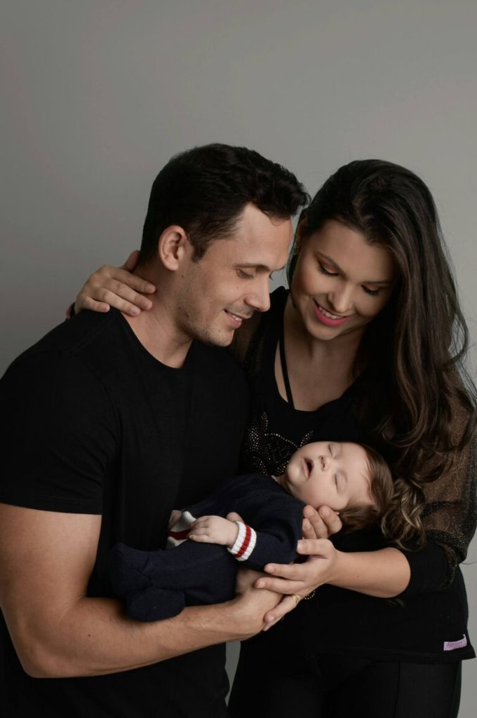 Föräldrar håller sin sovande bebis mot grå studiobakgrund, familjefoto i studio