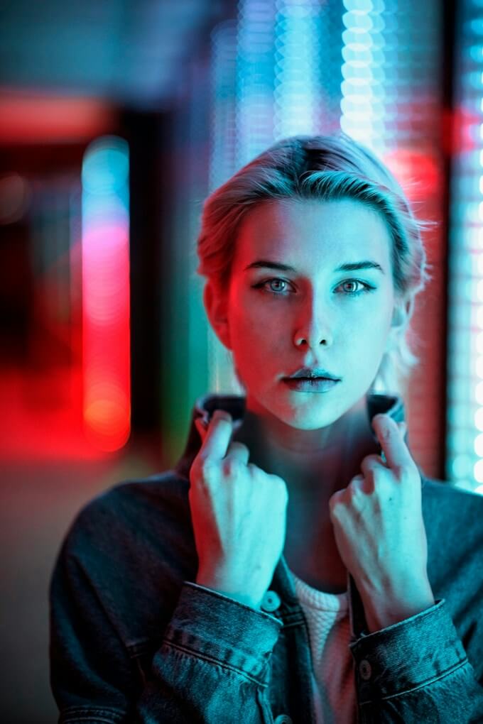 Blond modell i jeansjacka framför suddiga röda och blå ljus