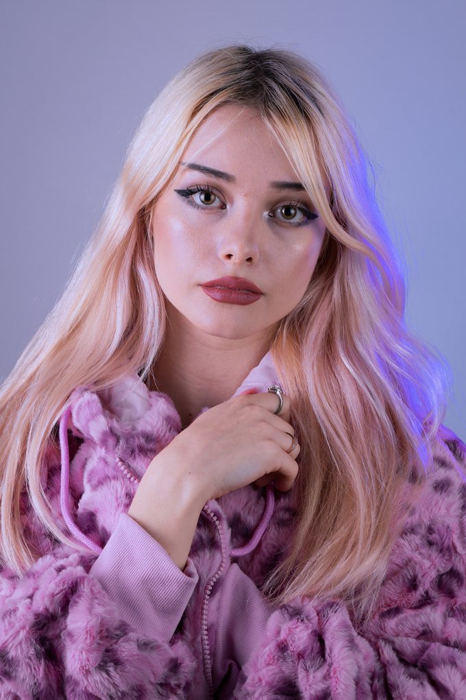 Kvinna med ljusrosa hår i lila färgljus och rosa pälsjacka