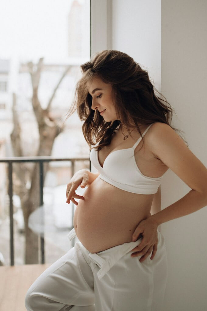 Gravid kvinna i vit topp vid fönster i naturligt ljus