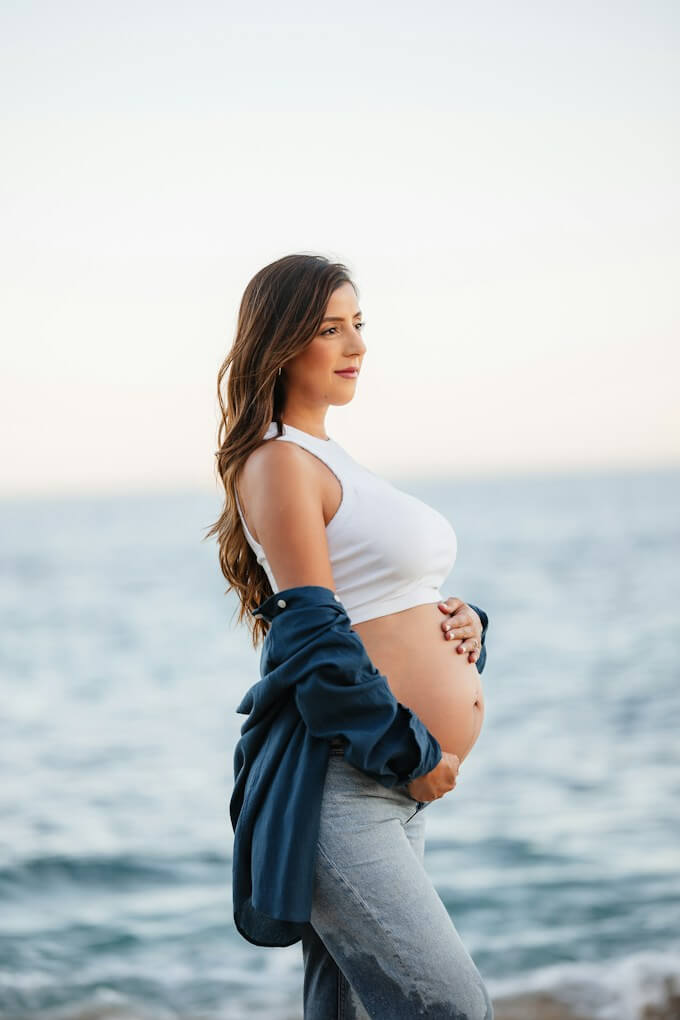Gravid kvinna i vit topp vid havet