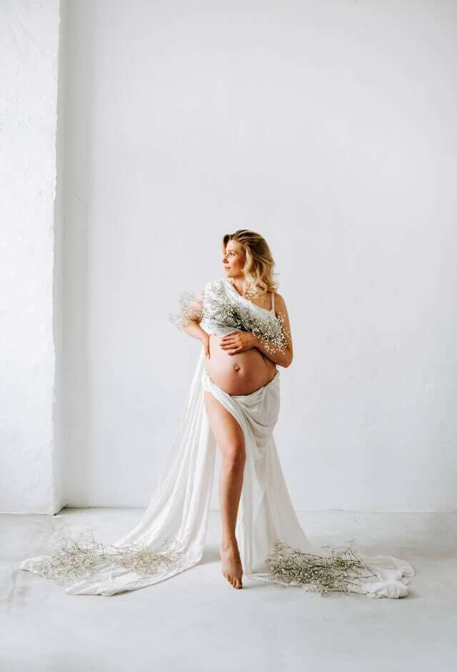 Gravid kvinna i vitt tyg med blombukett i ljus studio