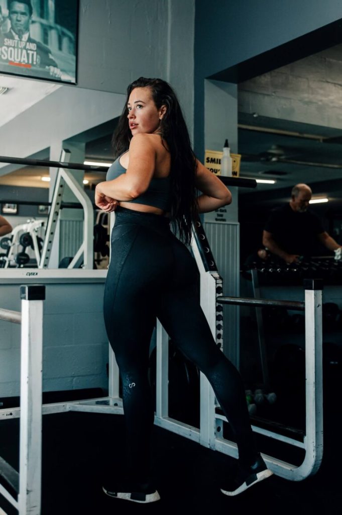 Kvinna i träningskläder poserar i gym med träningsmaskiner, modellfotograf Stockholm