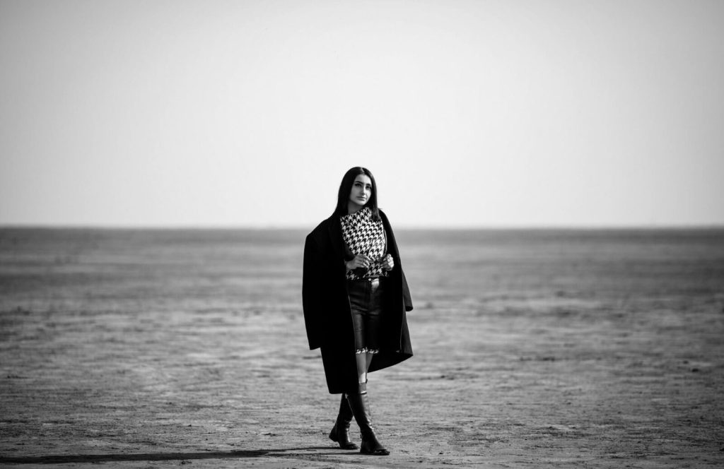 Svartvitt modefoto av kvinna i lång kappa på öppen strand