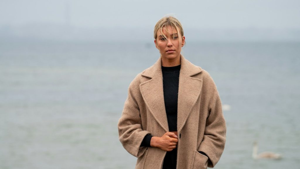 Kvinna i beige kappa vid havet en grå dag