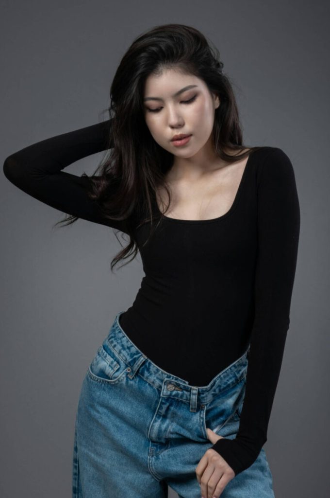 Kvinna i svart body och jeans med handen i håret i studio
