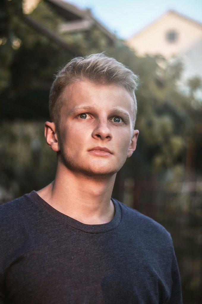 Ung man med kort ljust hår i mörk t-shirt utomhus