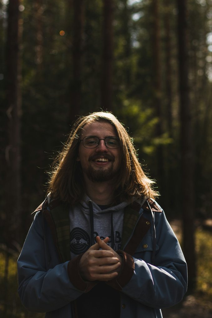 Leende man med långt hår och glasögon i en skog