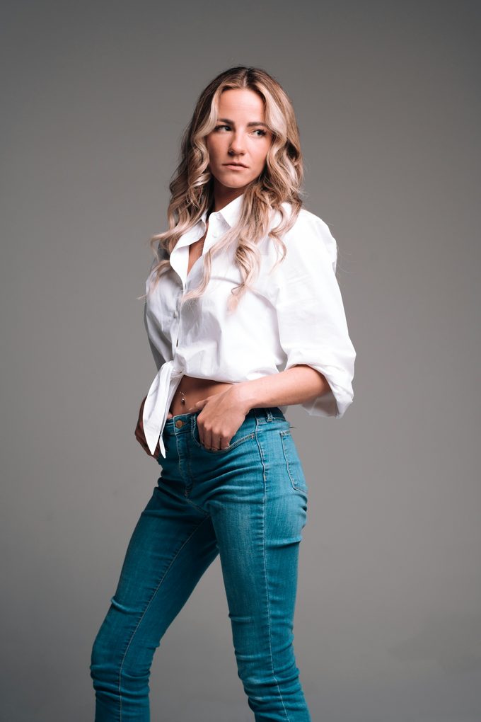 Blond modell i vit skjorta och jeans mot grå studiovägg
