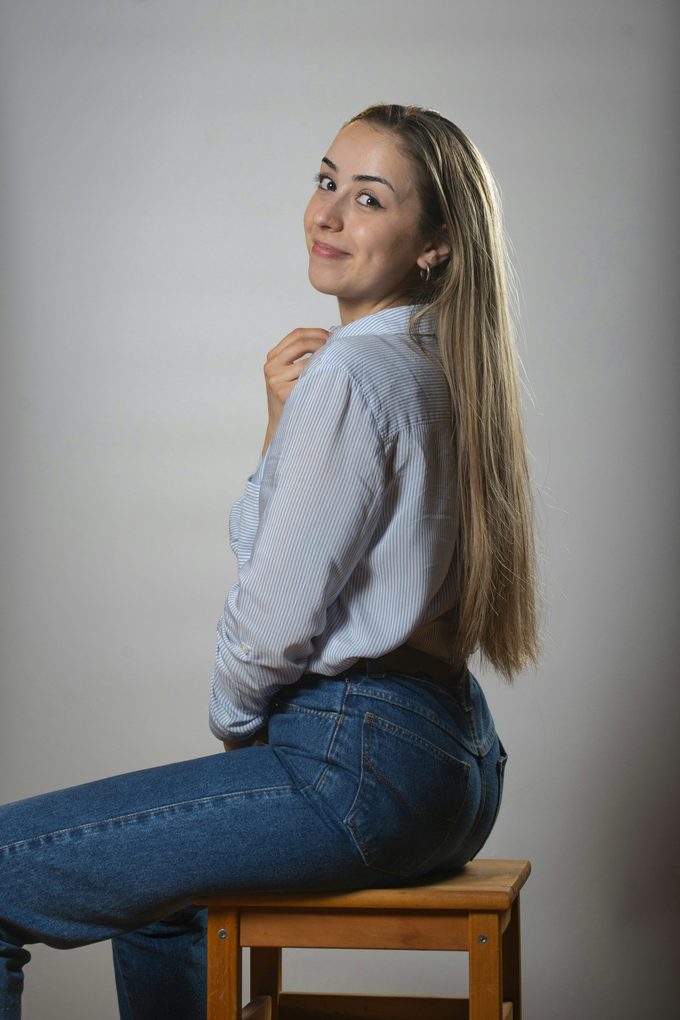 Långhårig blond modell i ljusblå skjorta och jeans sitter på pall