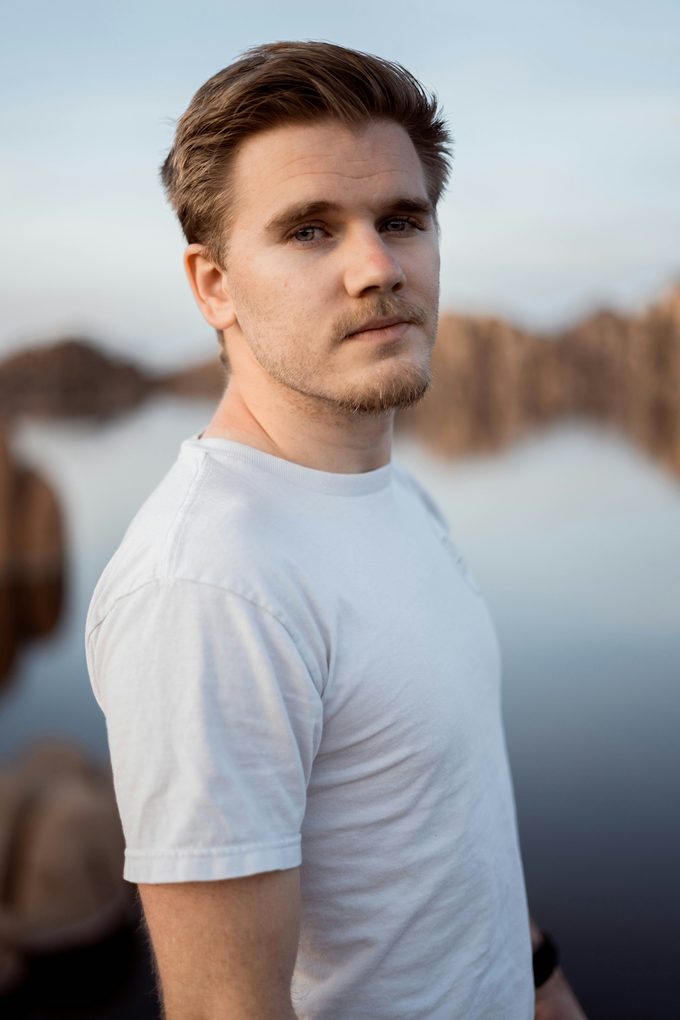 Man i vit t-shirt vid stilla sjö i mjukt kvällsljus