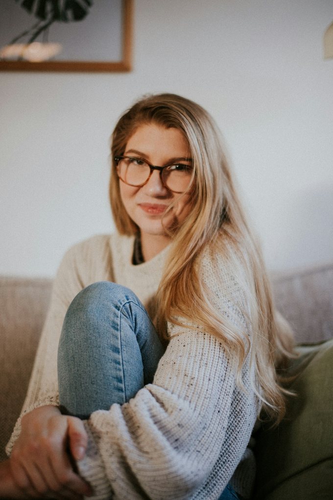 Kvinna med glasögon och stickad tröja sitter i en soffa hemma
