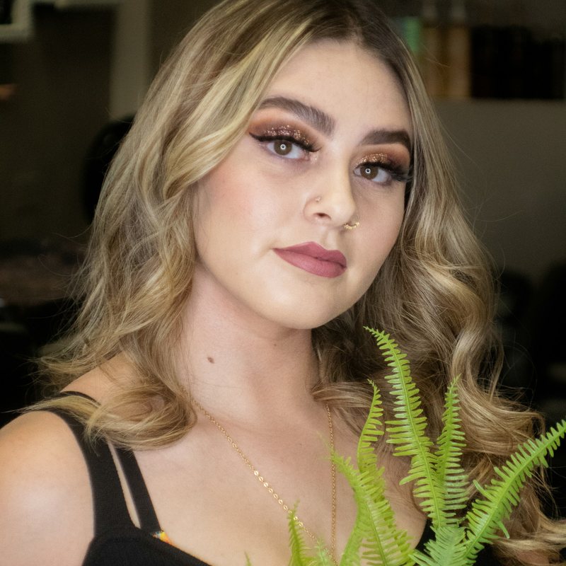 Blond kvinna med professionell makeup bredvid en ormbunke