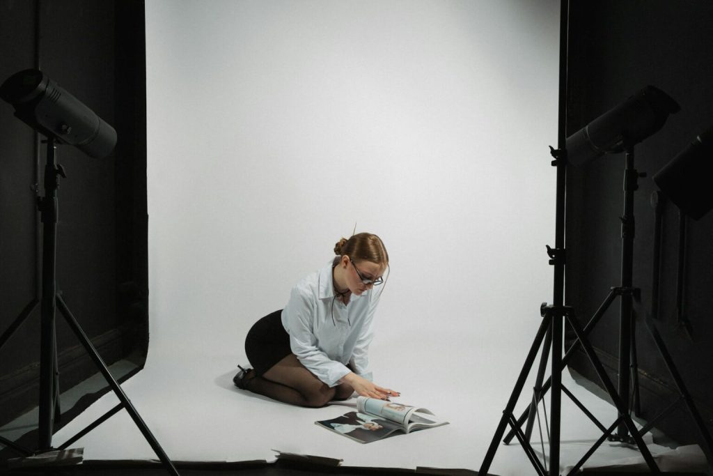 Kvinna bläddrar i fotobok på golvet i vit studio med lampor