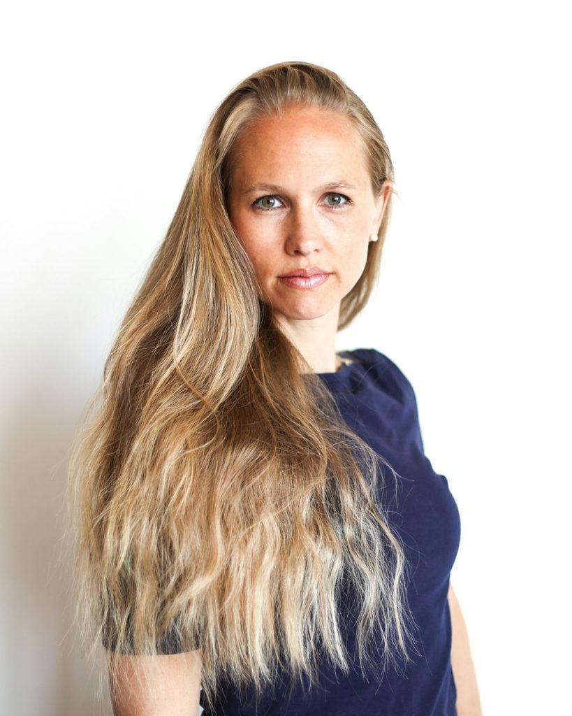 Kvinna med långt ljust hår i mörkblå tröja mot vit bakgrund