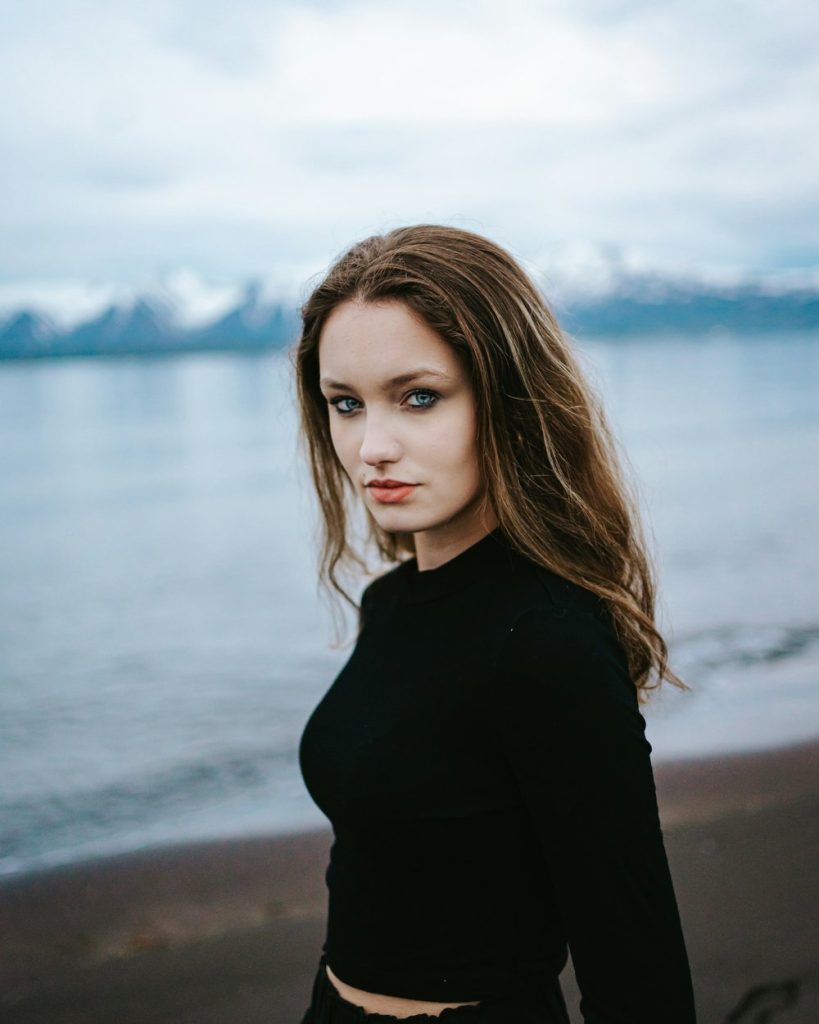 Kvinna i svart tröja på en strand med snöklädda berg