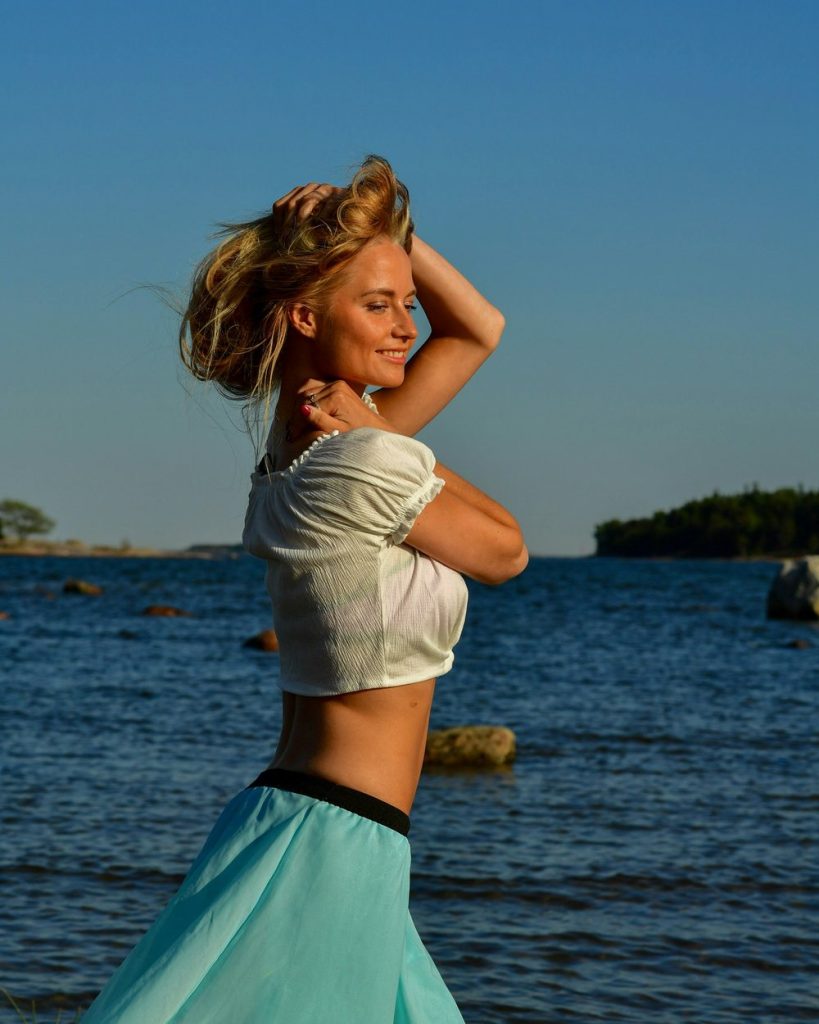 Blond kvinna i vit topp och turkos kjol dansar vid havet