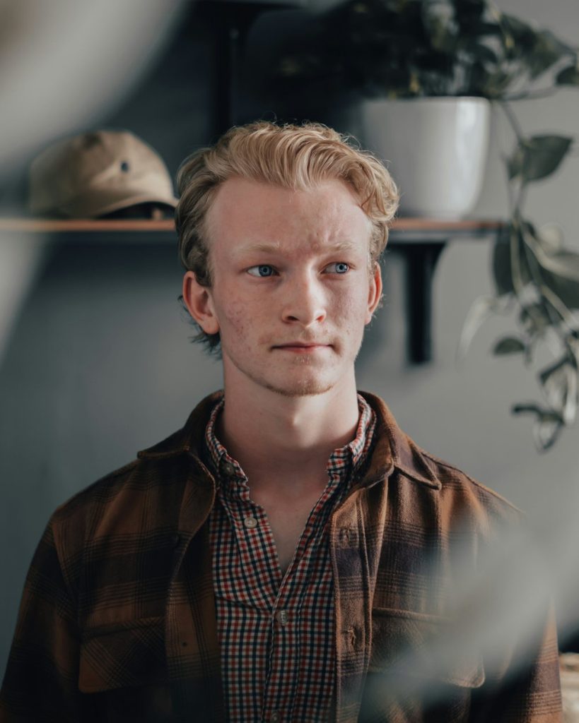 Ung man med ljust hår i rutig skjorta framför hyllor med växter
