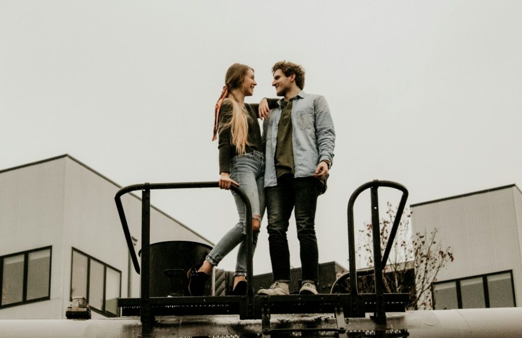 Par står på industritak mot grå himmel, modellfotograf Stockholm