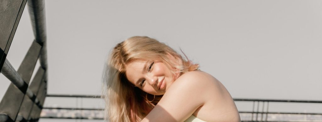 Leende blond kvinna sitter på en takterrass i solljus