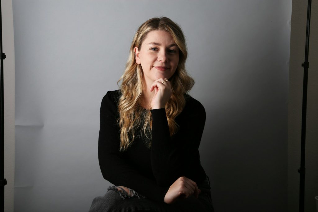 Kvinna med långt ljust hår i svart tröja sitter i en fotostudio