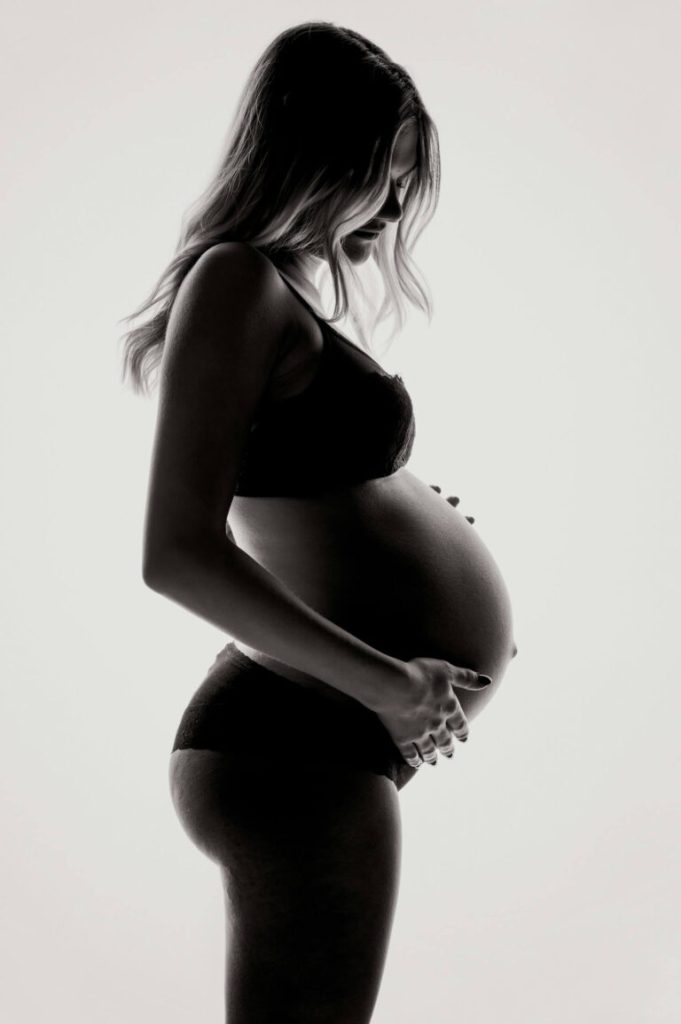 Gravid kvinna i siluett i profil mot ljus bakgrund