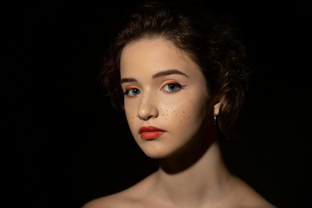 Ung kvinna med fräknar och orange eyeliner i lågmält ljus