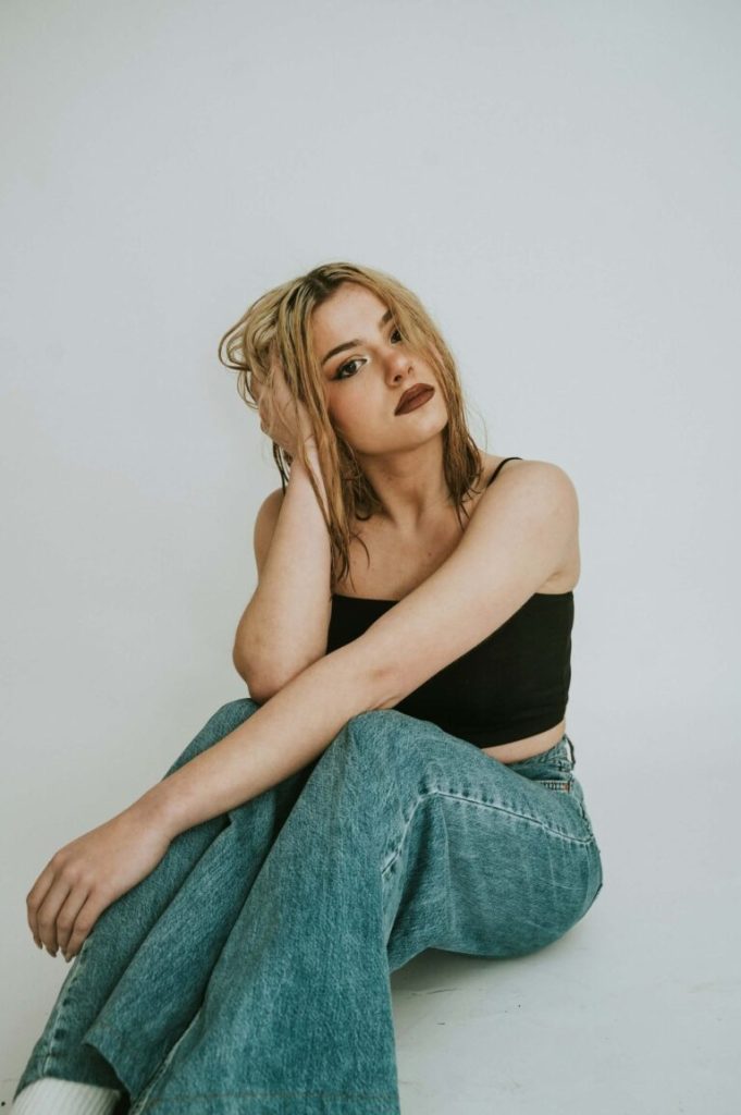 Kvinna i jeans och svart topp sitter på golvet i studio