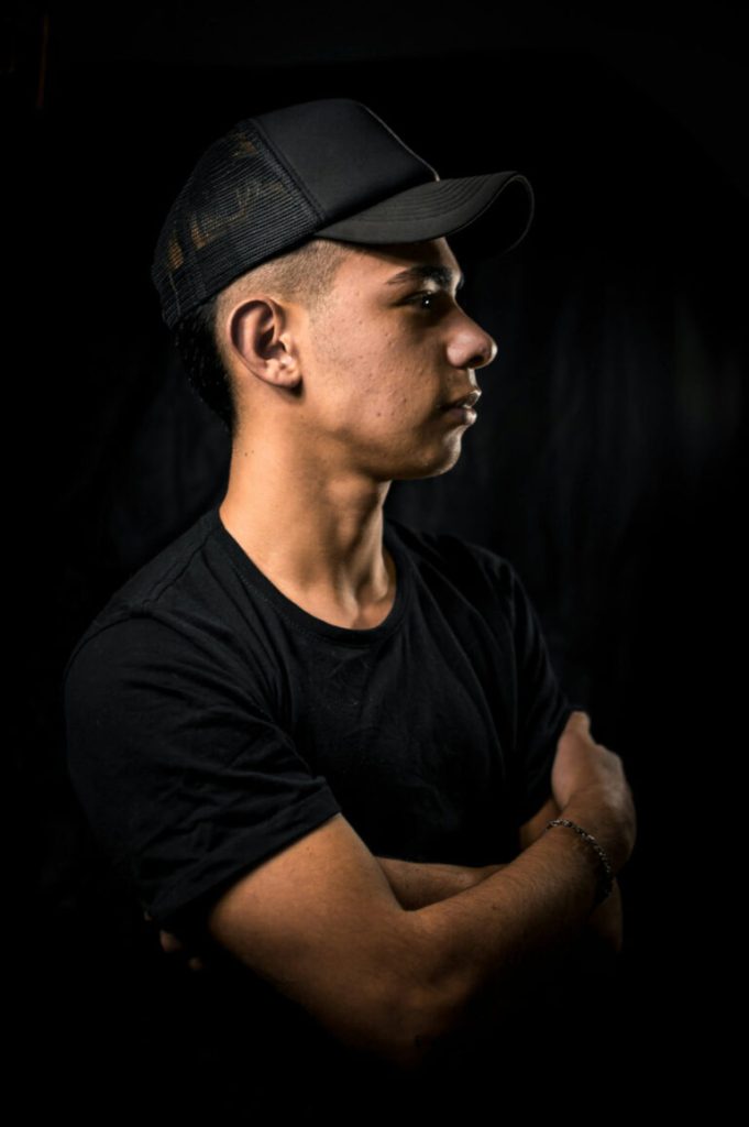 Man i keps och svart t-shirt i profil mot mörk bakgrund
