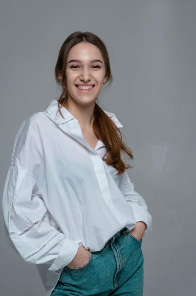 Leende kvinna i vit skjorta och jeans mot grå bakgrund
